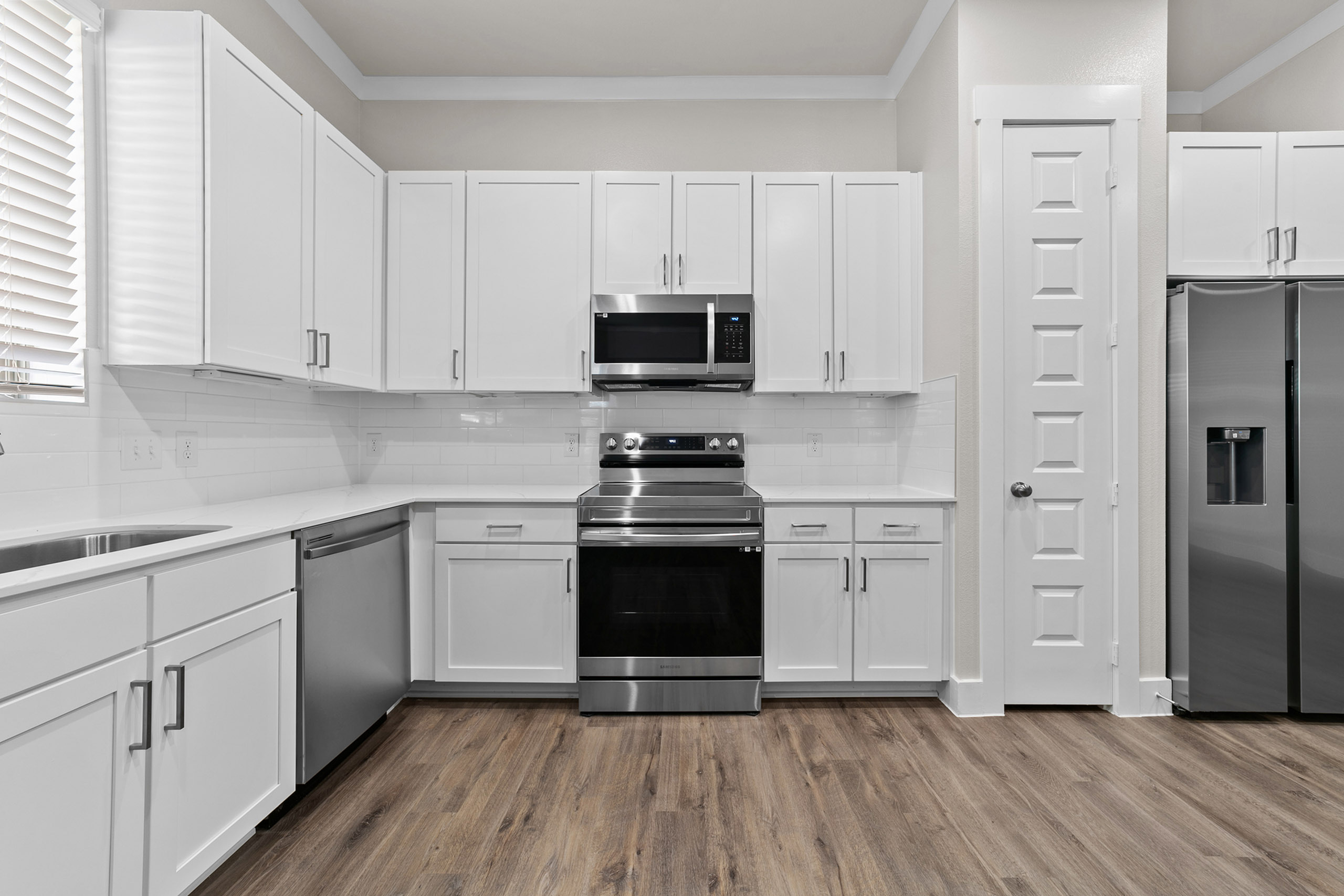 Modern kitchen with sleek stainless steel appliances, elegant white cabinetry, and stylish hardwood flooring.