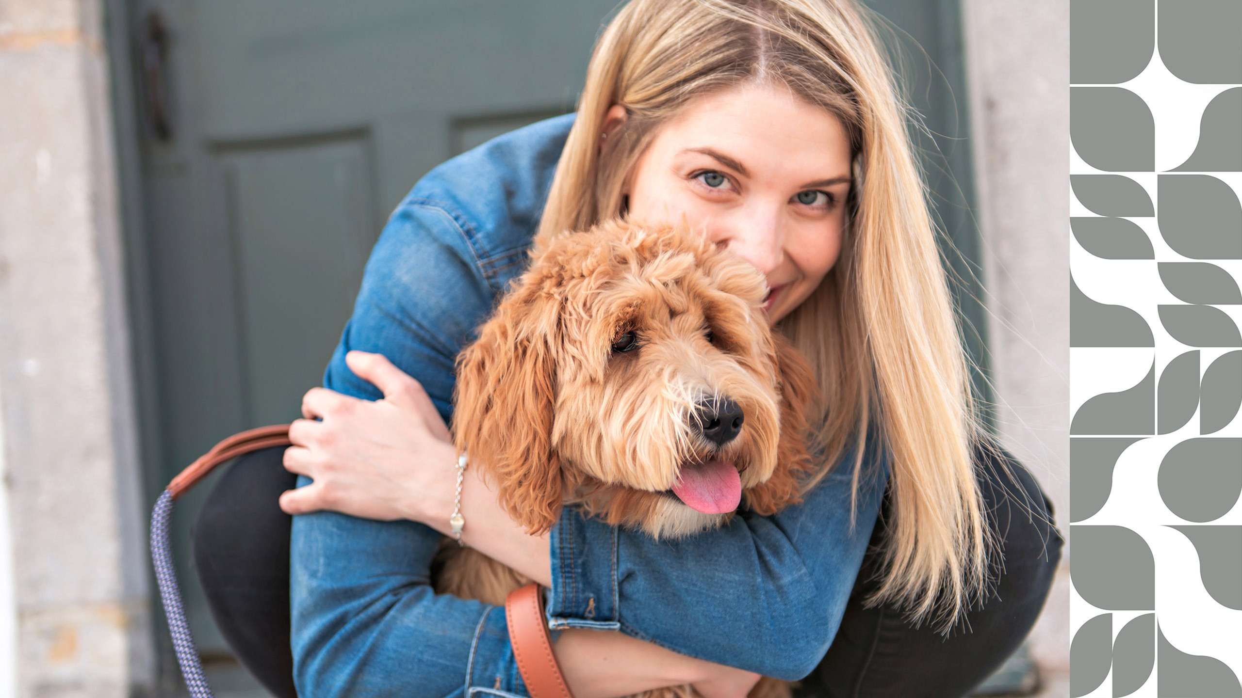 Woman joyfully hugging a fluffy dog in front of a stylish backdrop.