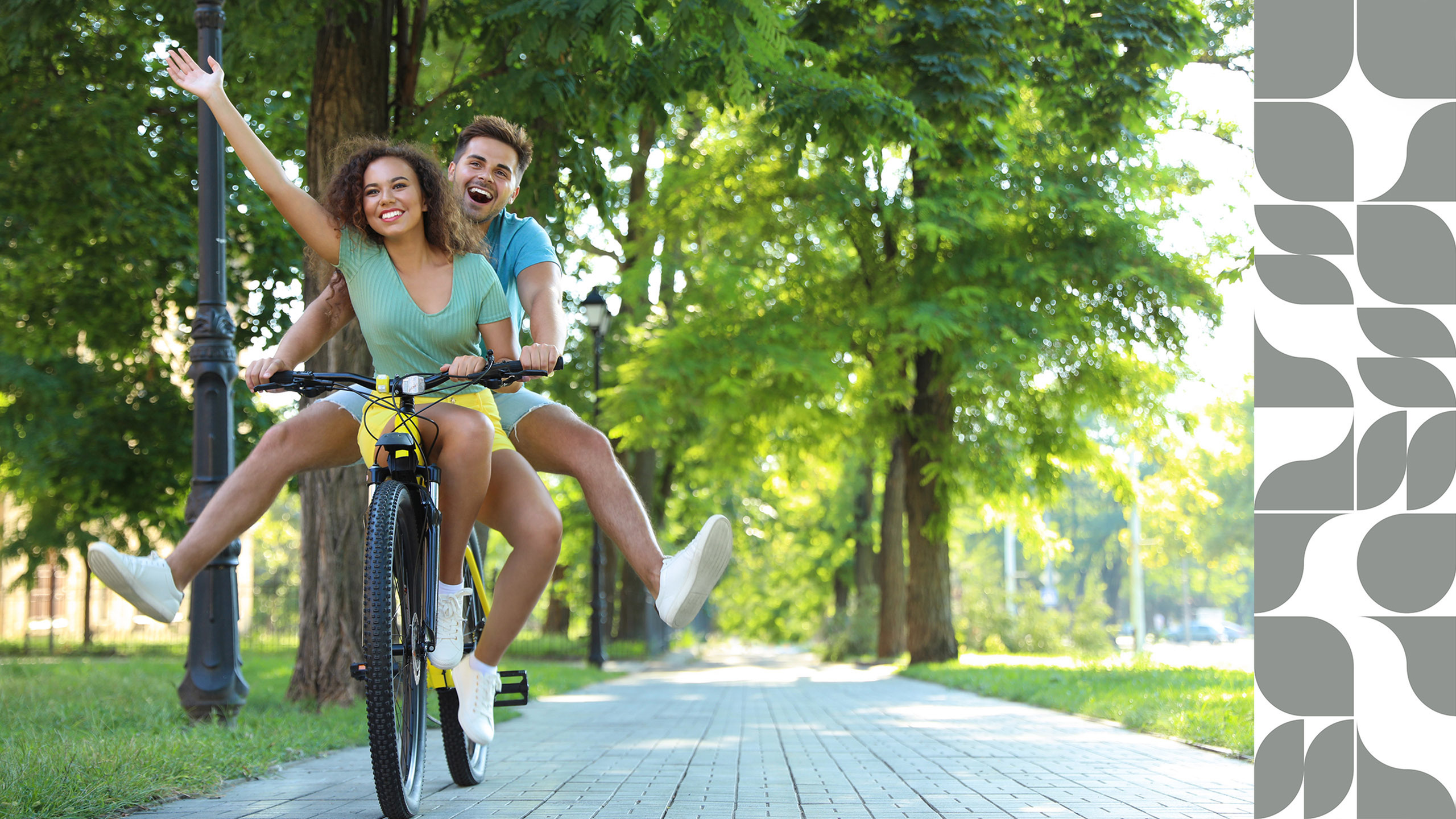 A cheerful couple cycling together on a tree-lined path in a sunny park.