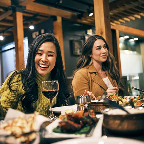 Vibrant dining scene with friends enjoying a delicious meal and wine in a cozy, stylish restaurant setting.