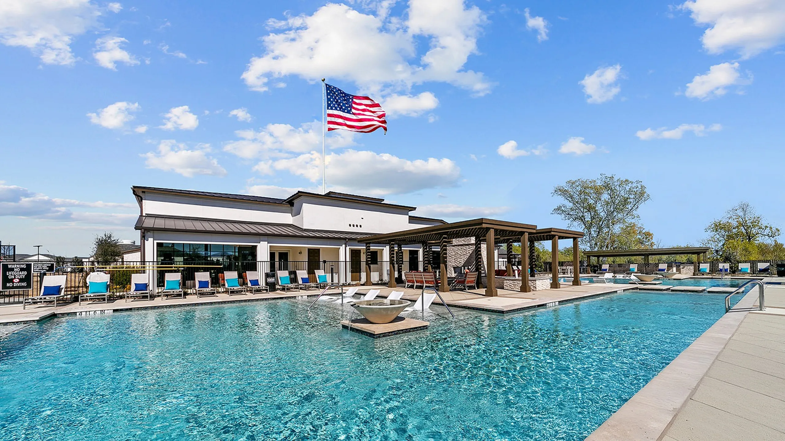 Luxurious outdoor pool area with sparkling blue water, stylish sun loungers, and modern clubhouse under a clear sky.