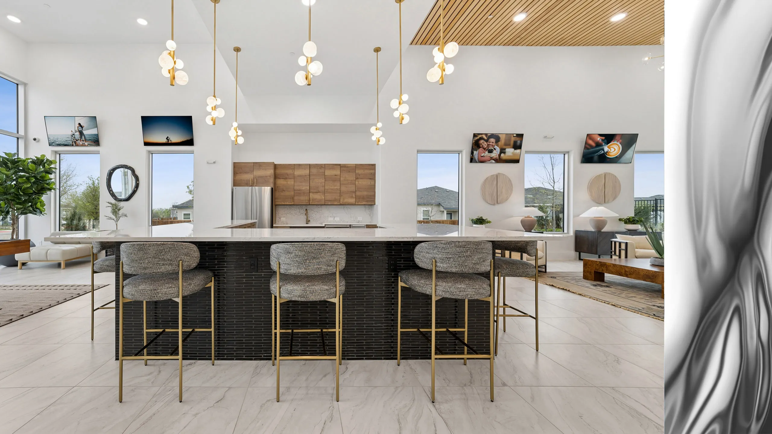 Luxurious open-plan clubhouse space featuring a sleek kitchen island, stylish modern lighting, and large windows with scenic views.