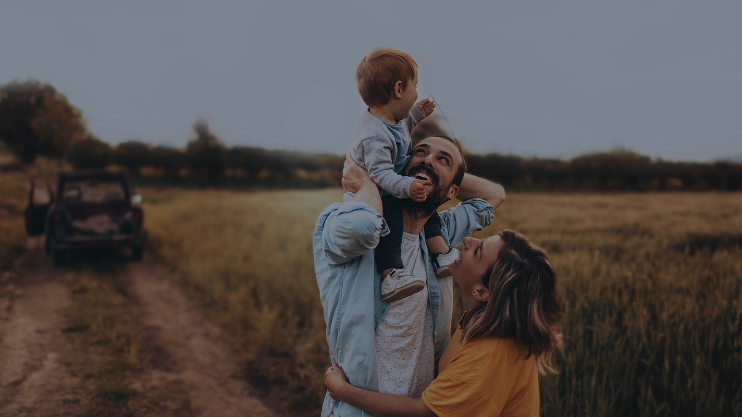 Joyful family enjoying a sunny day in a scenic field, with a blurred car in the background, capturing a perfect outdoor moment.