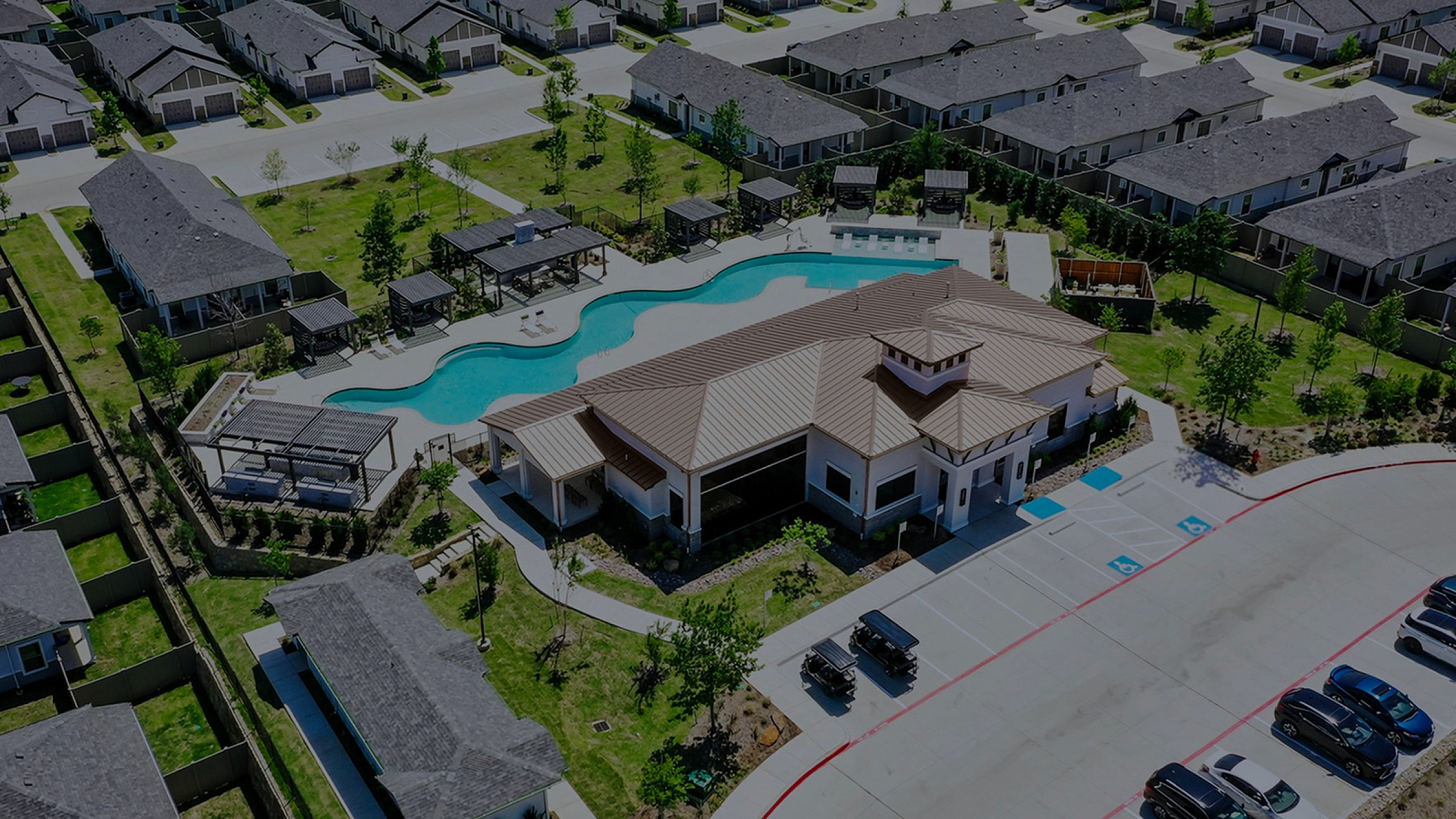 Aerial view of a modern housing community with a luxury clubhouse, elegant swimming pool, and landscaped green spaces.