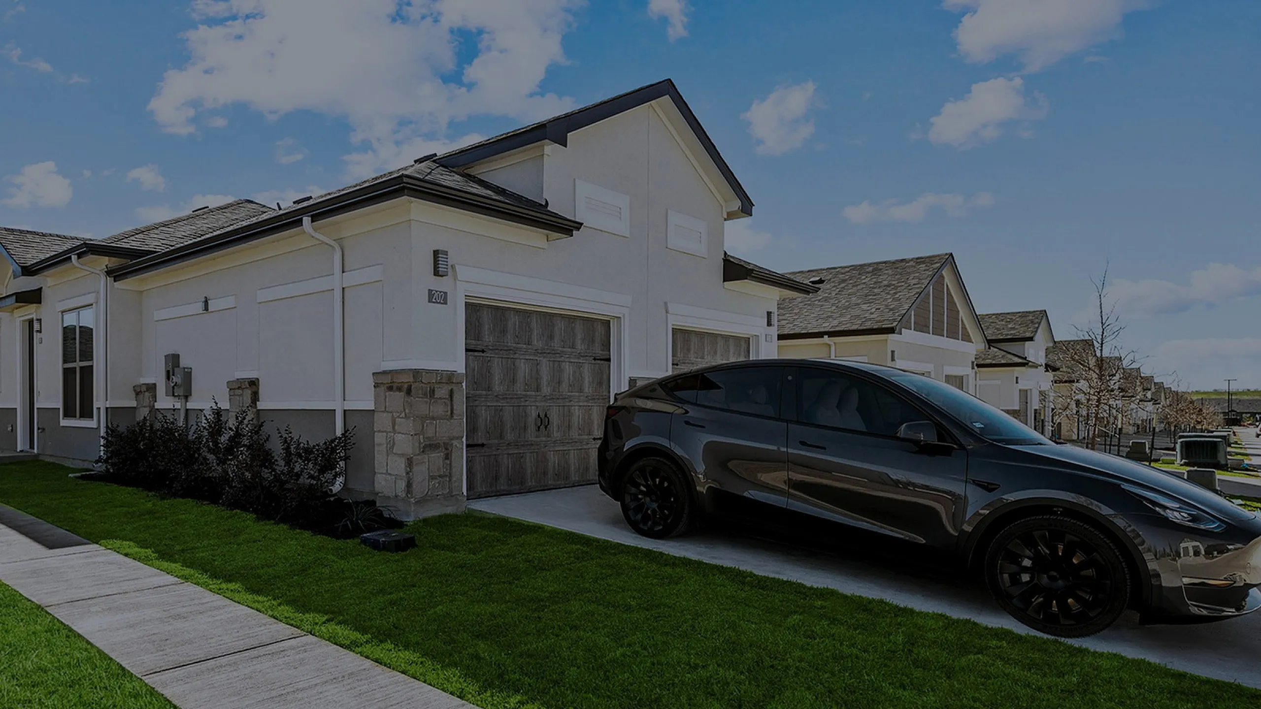 Charming modern home with a sleek black car in driveway, featuring a clean facade, lush green lawn, and a sunny sky backdrop.