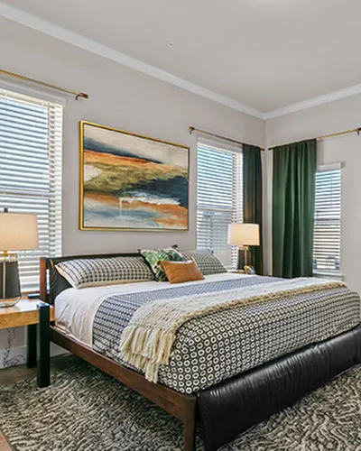Elegant bedroom with modern decor, featuring a comfortable bed, stylish lamps, and artistic wall painting amid abundant natural light.