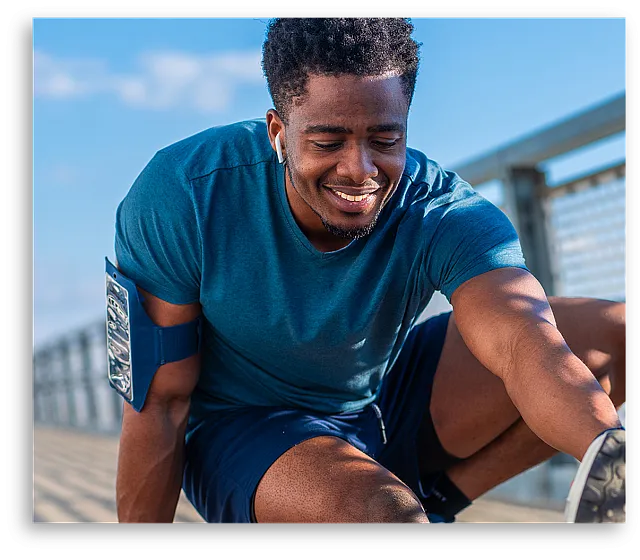 Energetic individual in sportswear smiling while stretching outdoors on a sunny day.