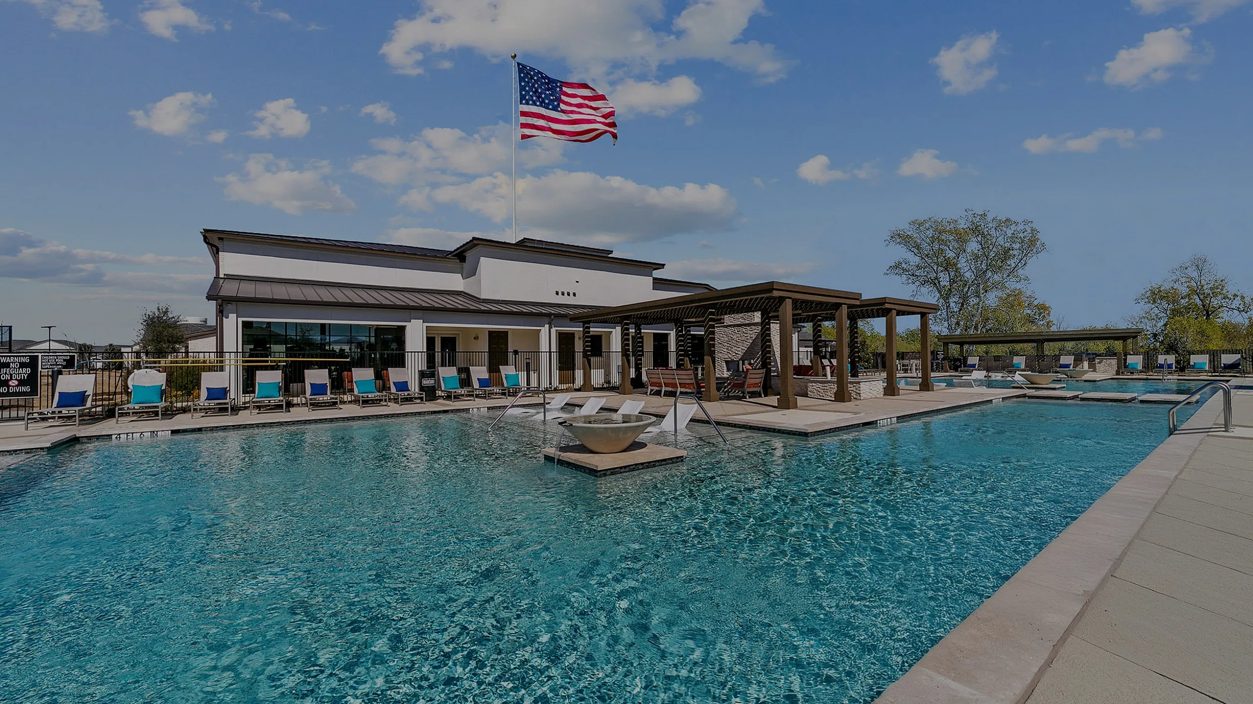 Inviting luxury pool area with lounge chairs, a sleek clubhouse, and clear blue skies, perfect for relaxation and entertainment.