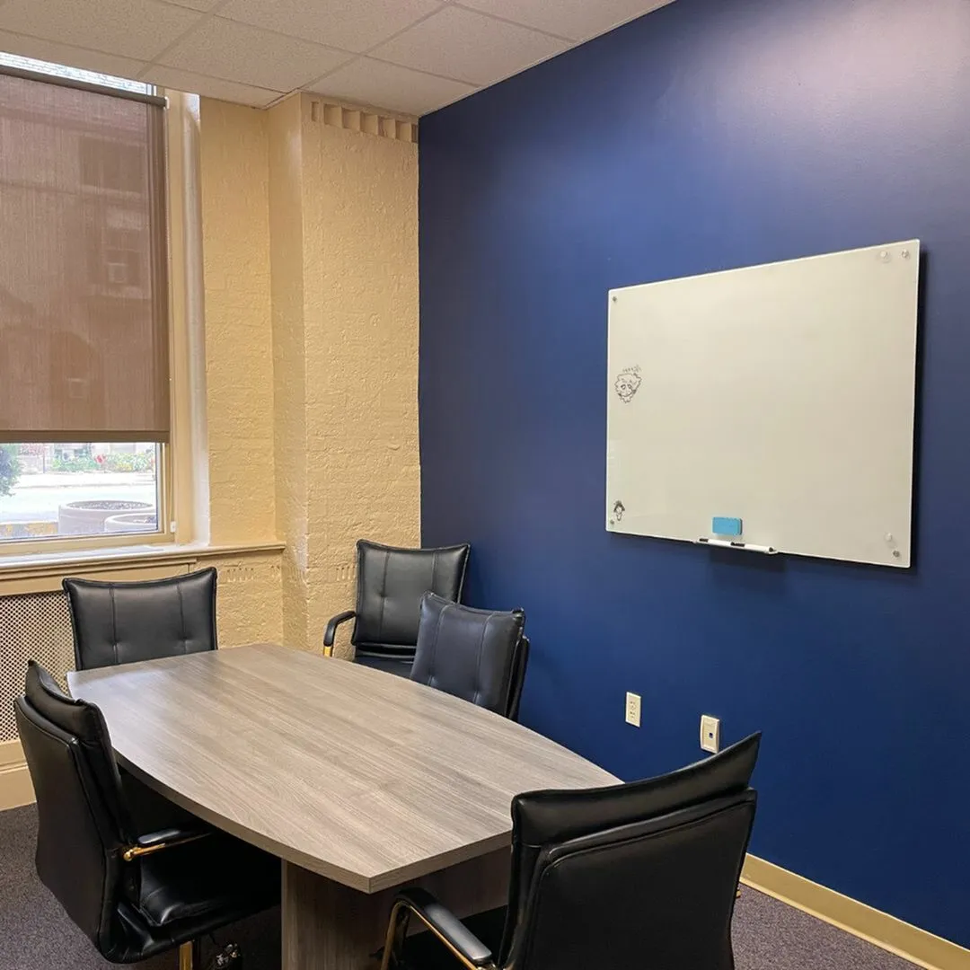Stylish office meeting room featuring a wooden table, four sleek chairs, and a modern blue accent wall.