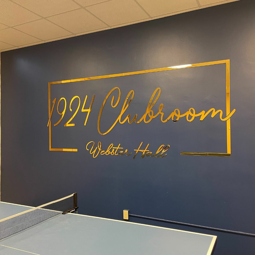 Elegant clubroom featuring stylish \'1924 Clubroom Webster Hall\' gold lettering on a navy wall with a ping pong table below.