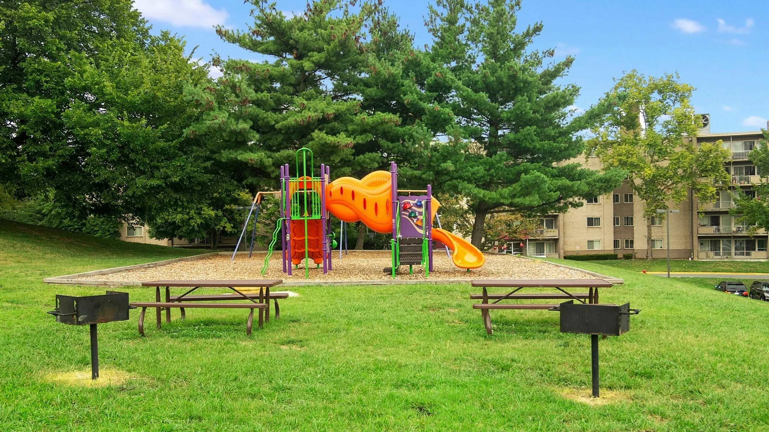 Charming playground nestled in a lush green park, featuring colorful slides and swings, perfect for family fun in a tranquil apartment community setting.