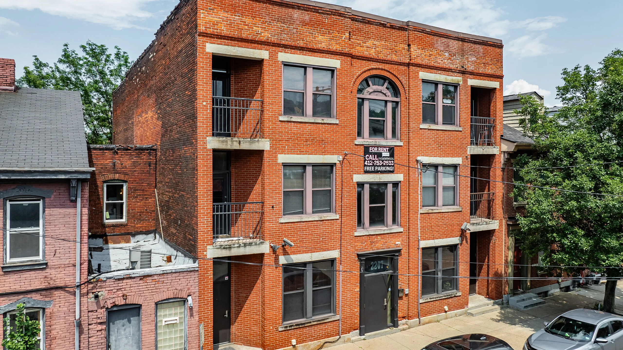 Charming brick apartment building with large windows and private balconies, offering rental opportunities with free parking in a vibrant neighborhood.