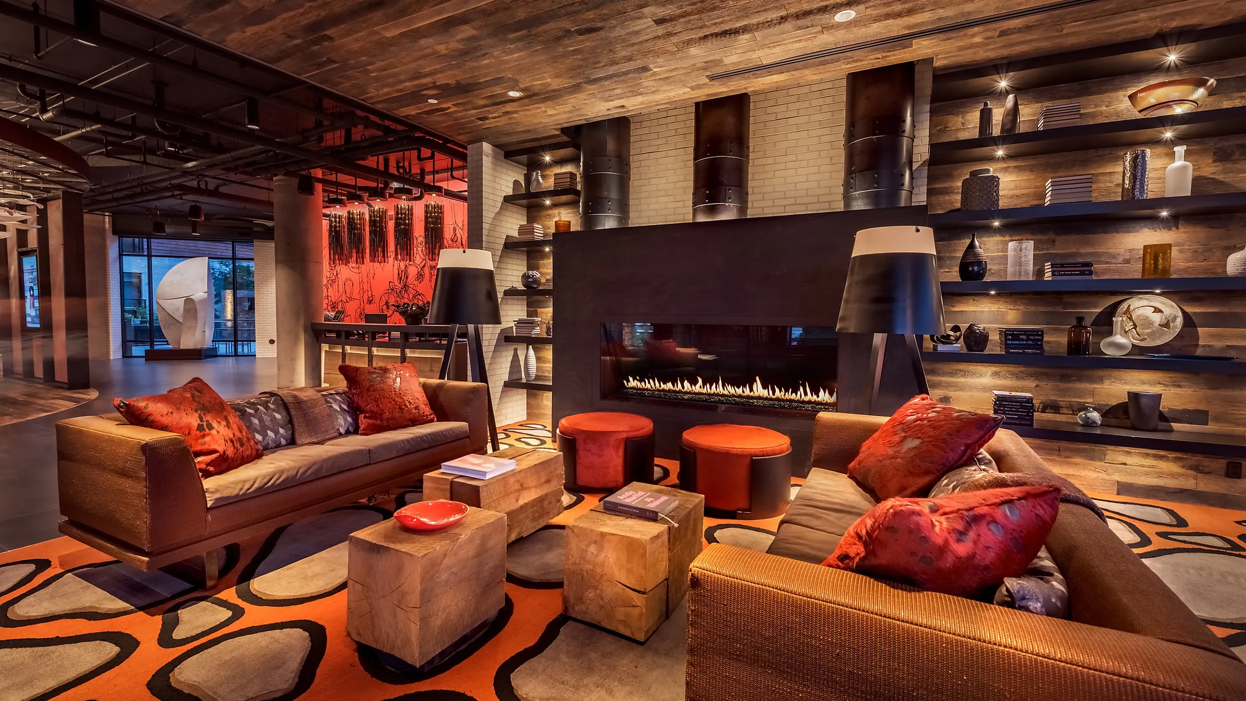 Luxurious lounge boasting a modern fireplace, stylish seating with vibrant cushions, and eclectic shelving against a rustic wood backdrop.
