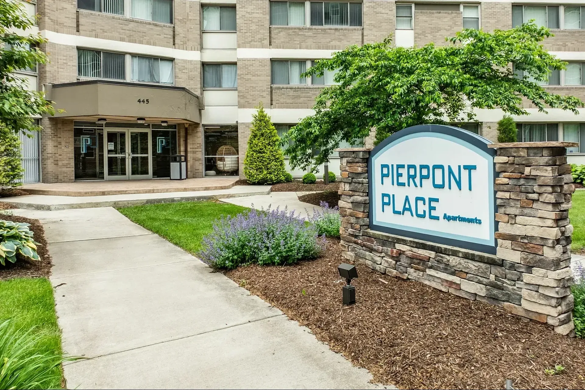 Aerial view of a vibrant apartment complex with ample parking, lush greenery, and panoramic views of a charming neighborhood, perfect for urban living.