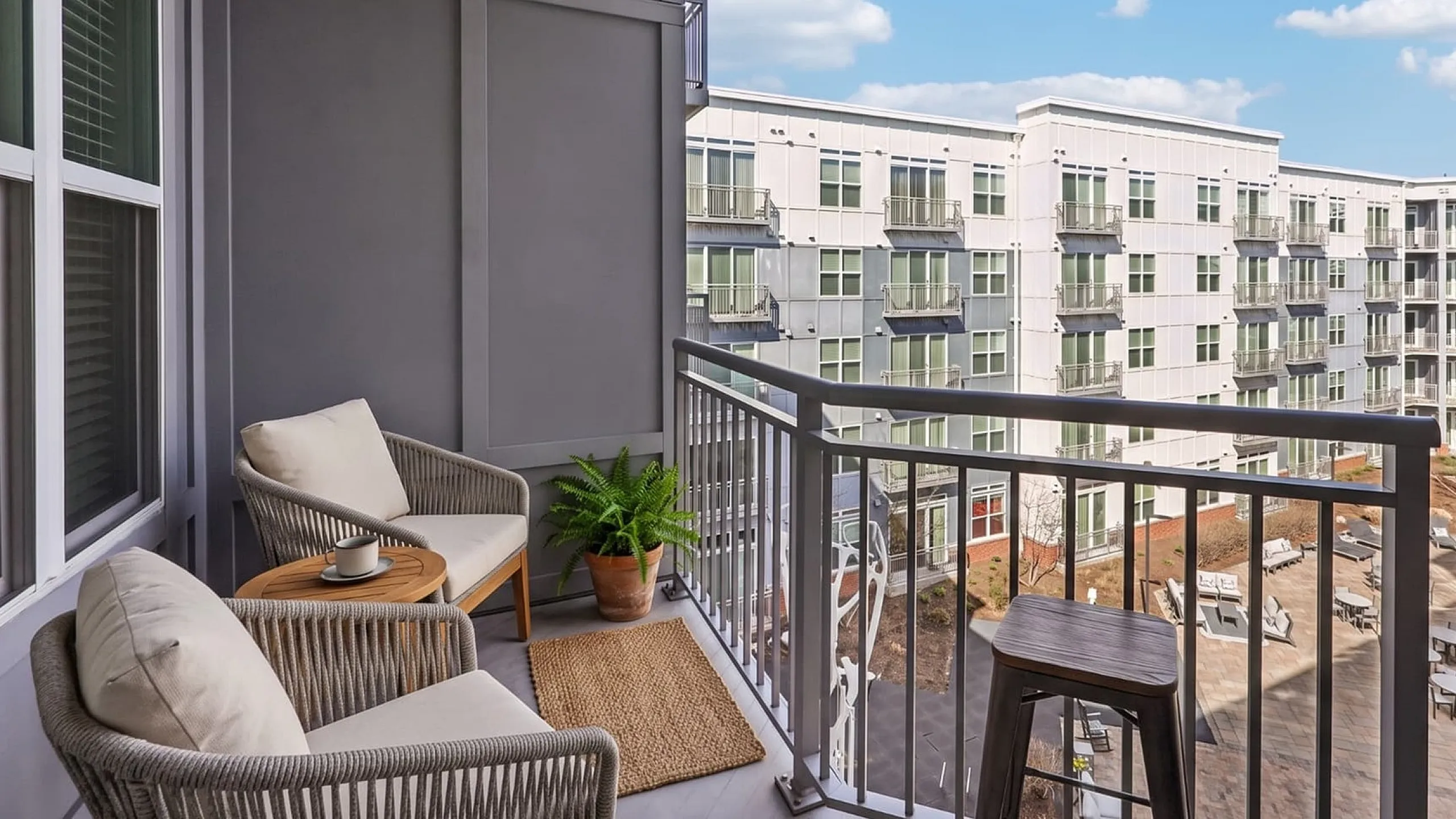 Charming balcony with cozy seating, overlooking a modern apartment complex under a sunny sky.