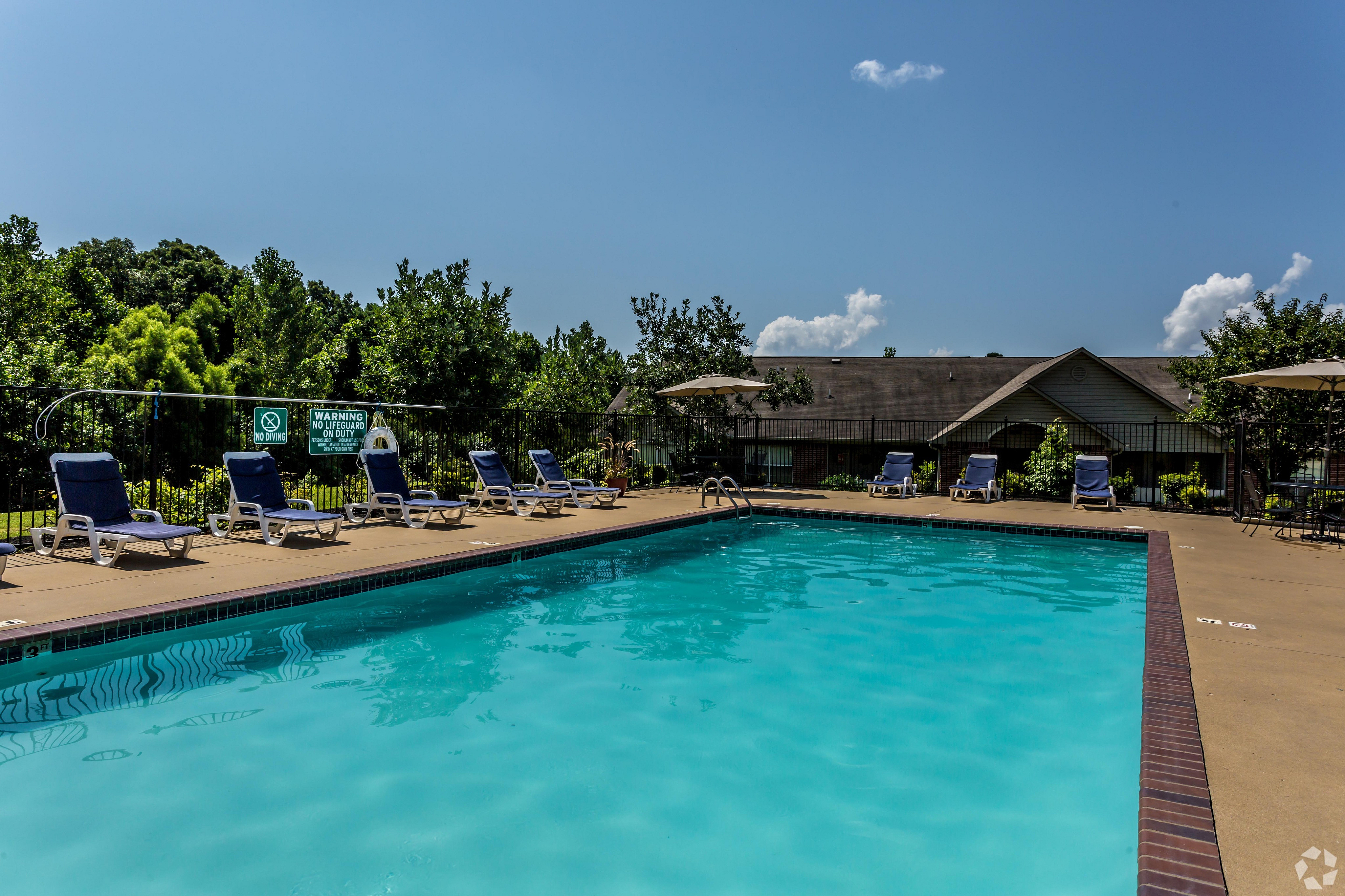 Inviting outdoor pool area with sun loungers and lush greenery on a sunny day.