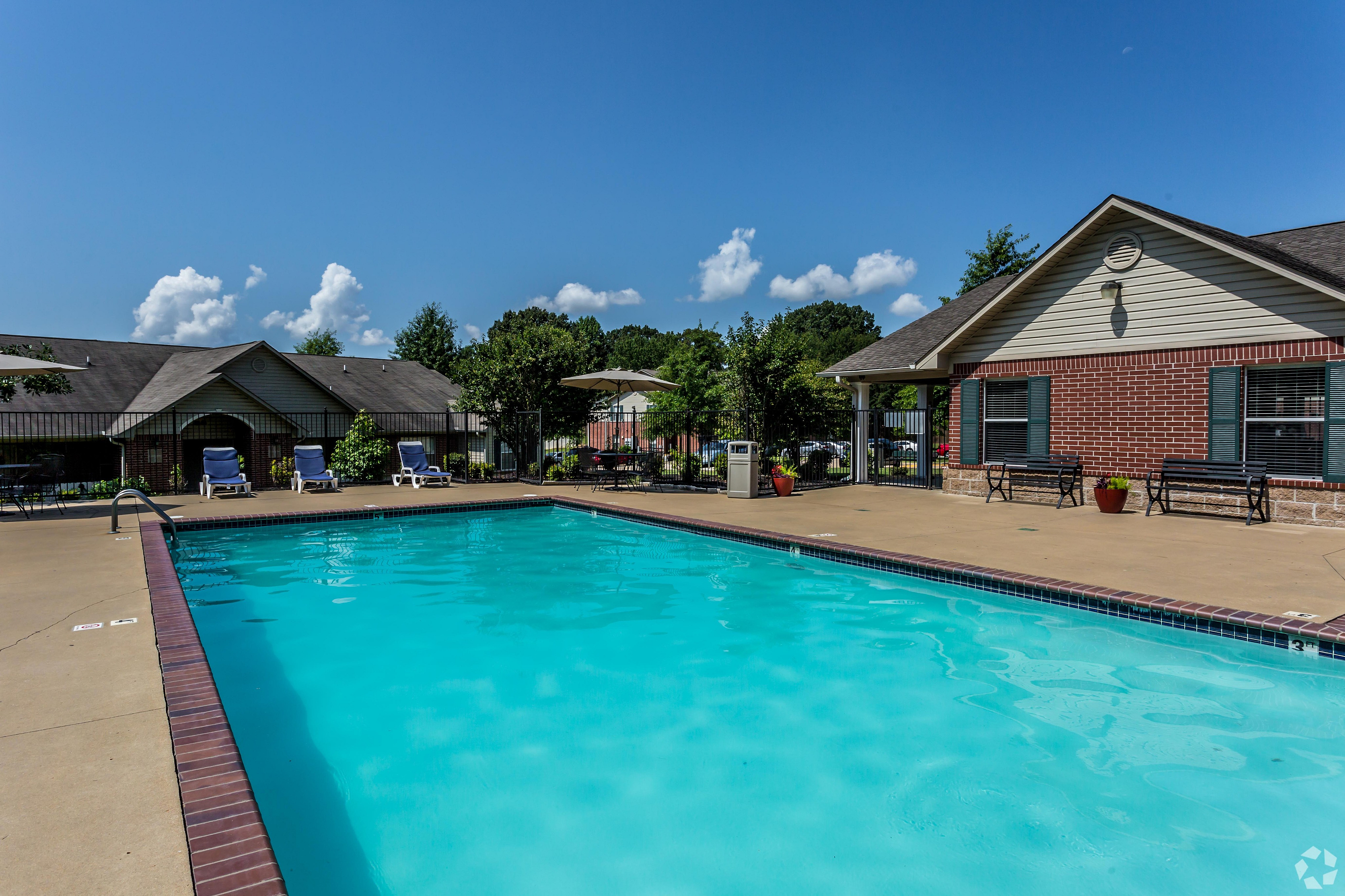 Inviting outdoor pool with turquoise water surrounded by lounge chairs and manicured greenery under a clear blue sky.