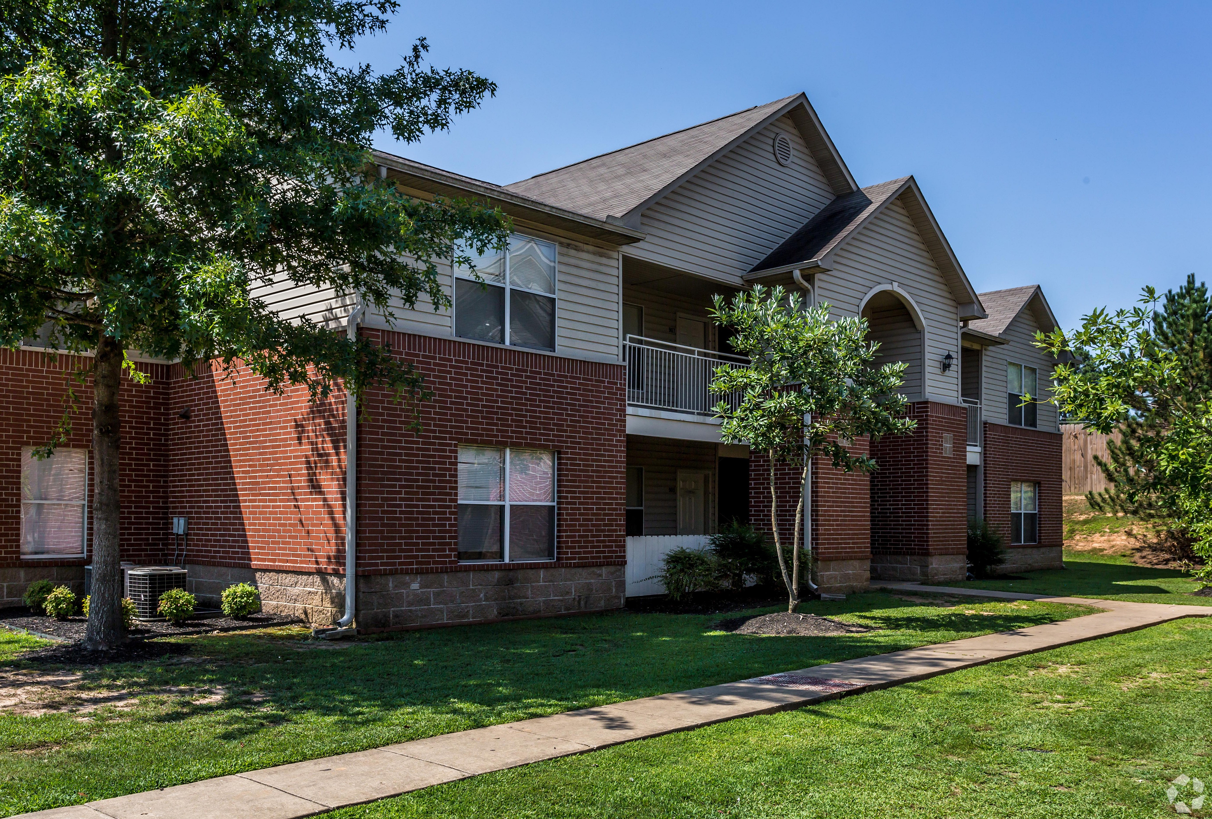 Beautiful brick and siding apartment building surrounded by lush green landscaping.