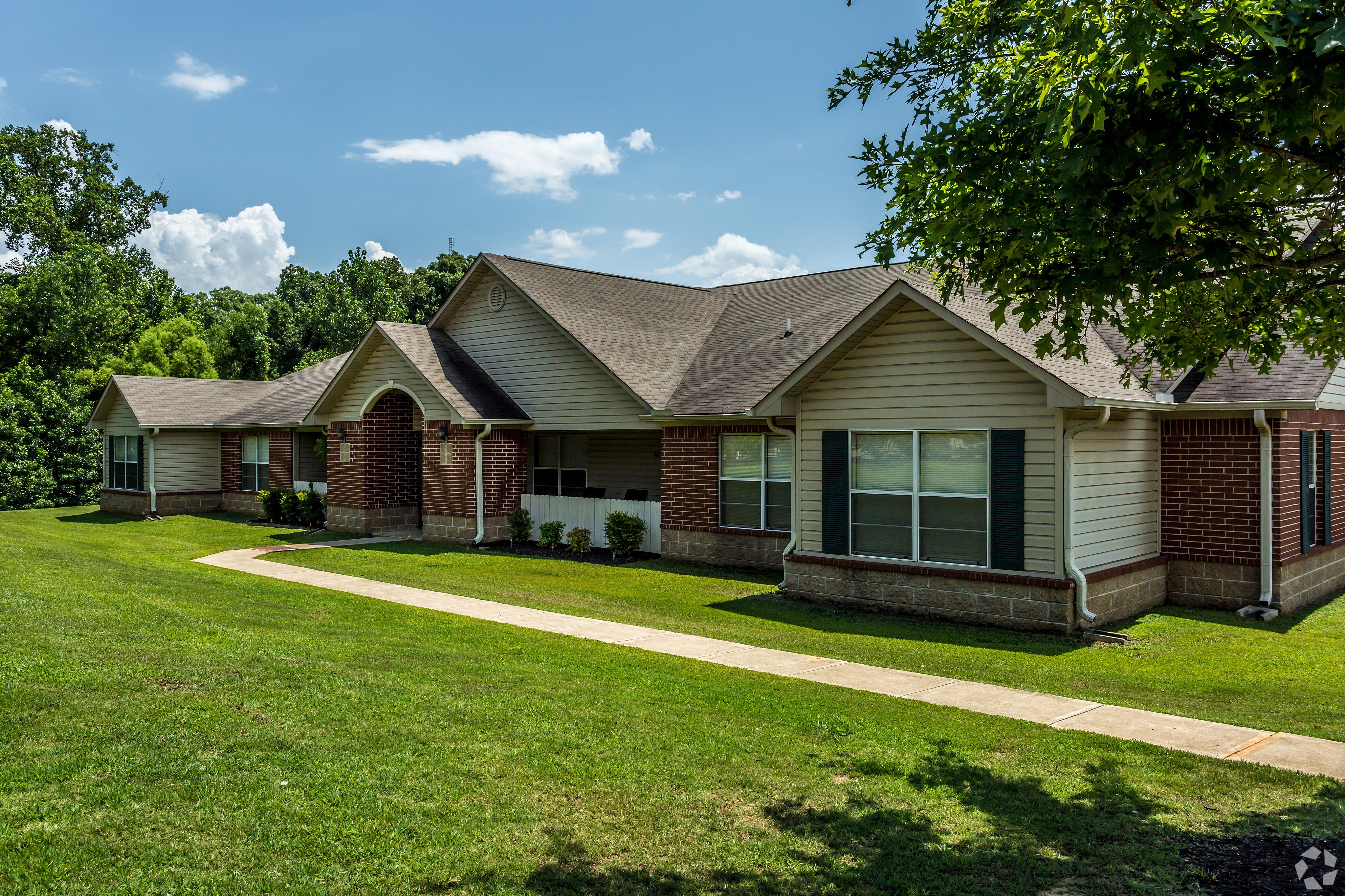 Picturesque single-story brick house with a lush green lawn, nestled among trees on a sunny day.