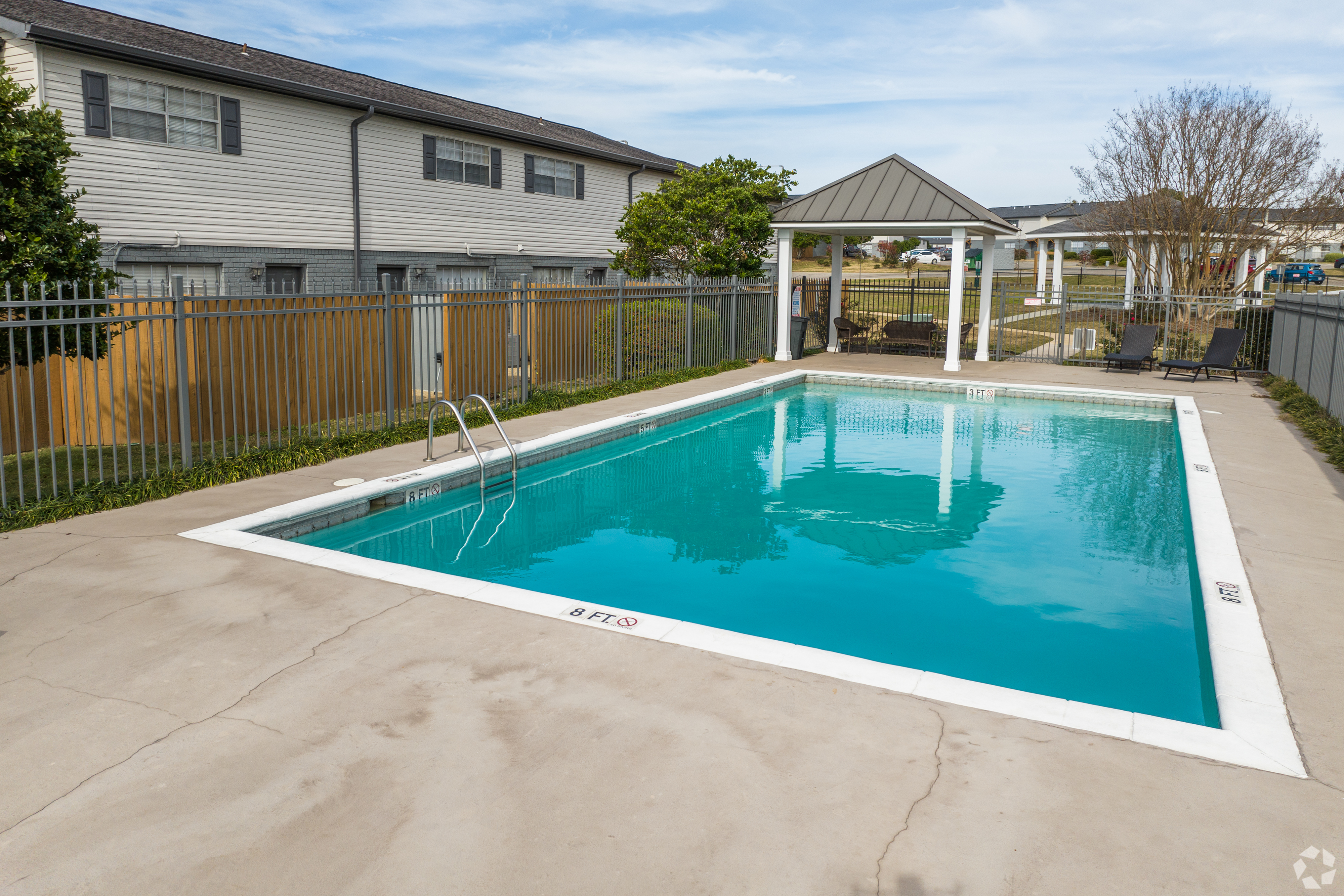 Charming outdoor pool with clear blue water and cozy seating under a gazebo.