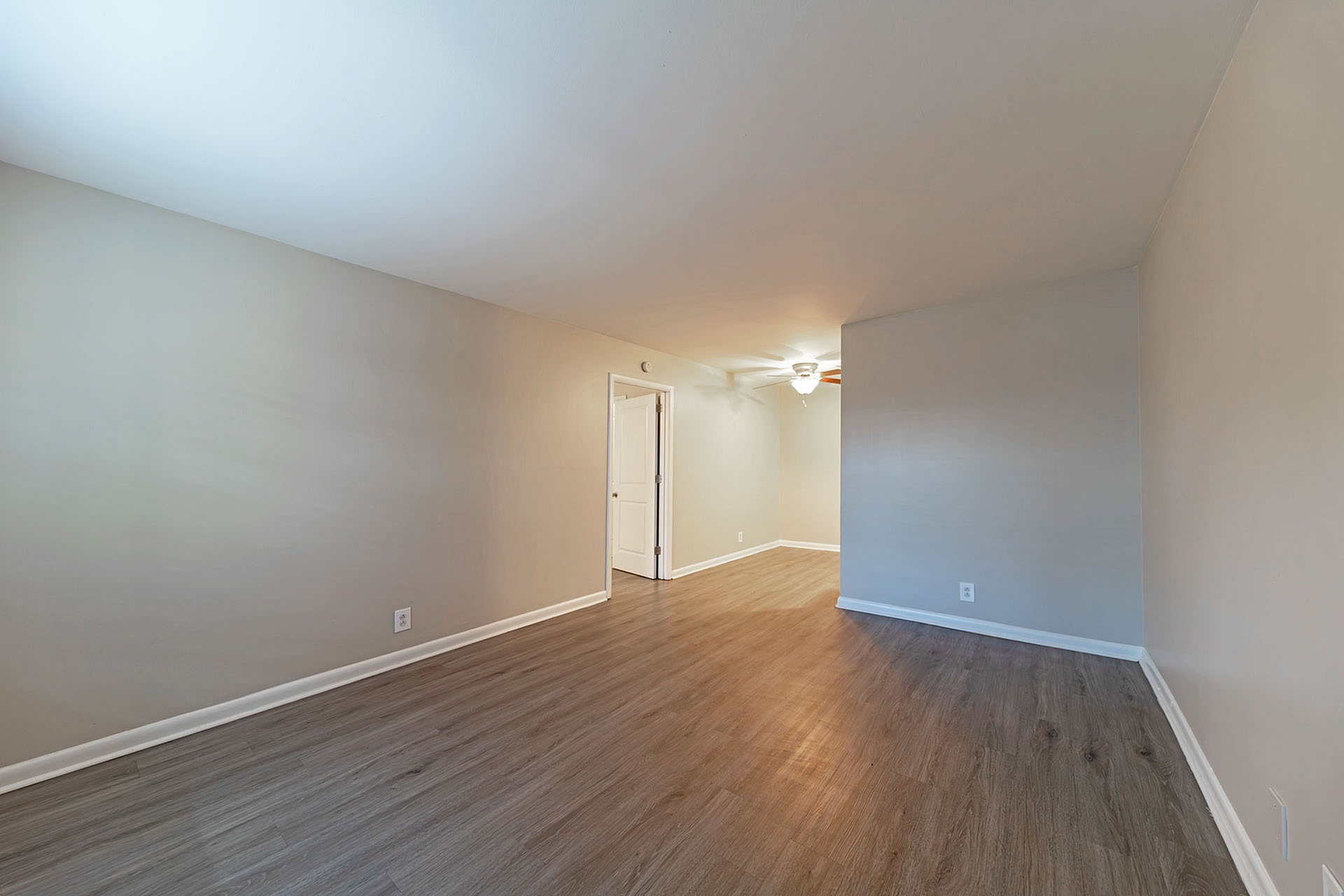 Bright, empty room with wood flooring, soft beige walls, and a ceiling fan.