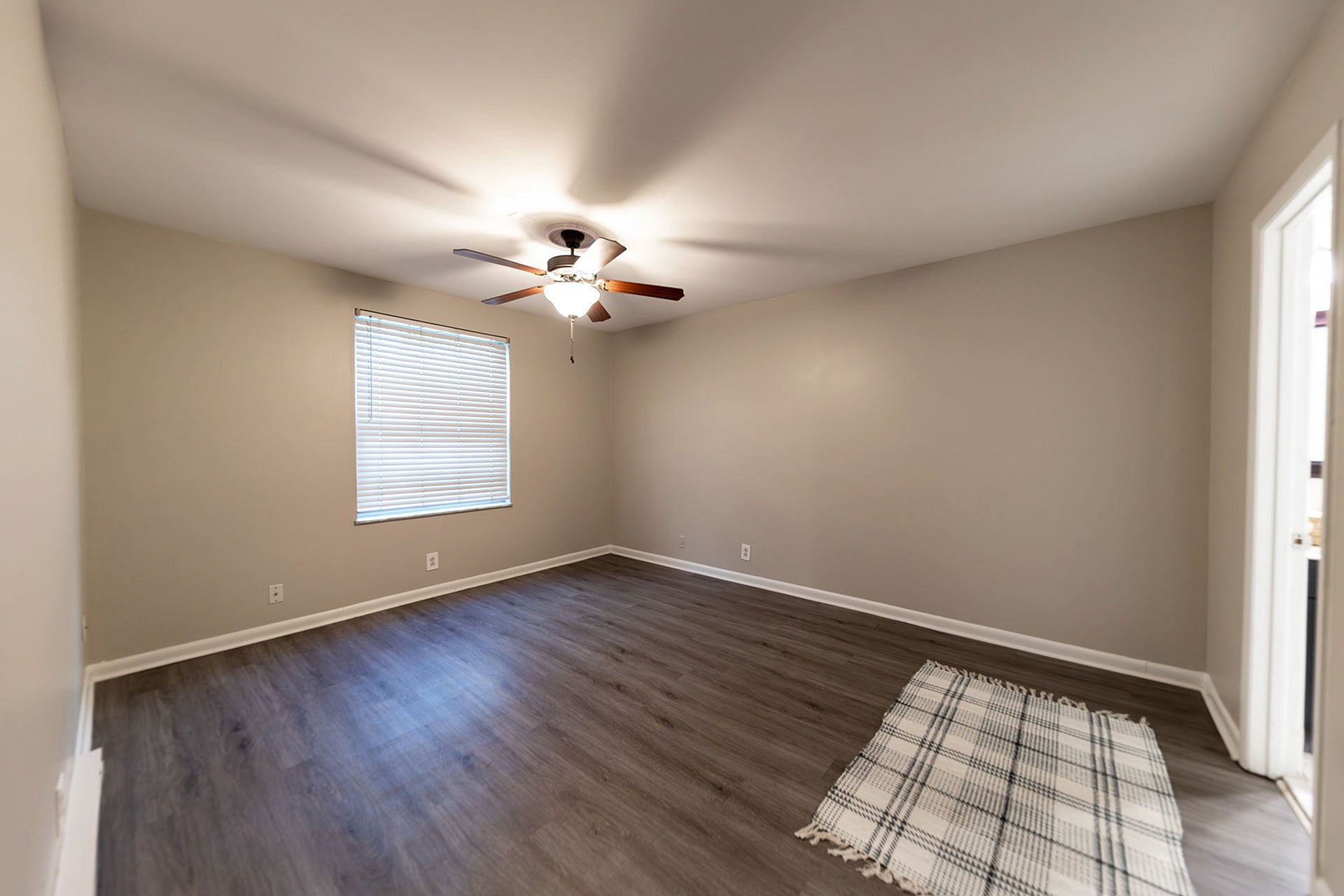 Spacious bedroom with elegant wooden flooring and ceiling fan, featuring a large window for ample natural light.