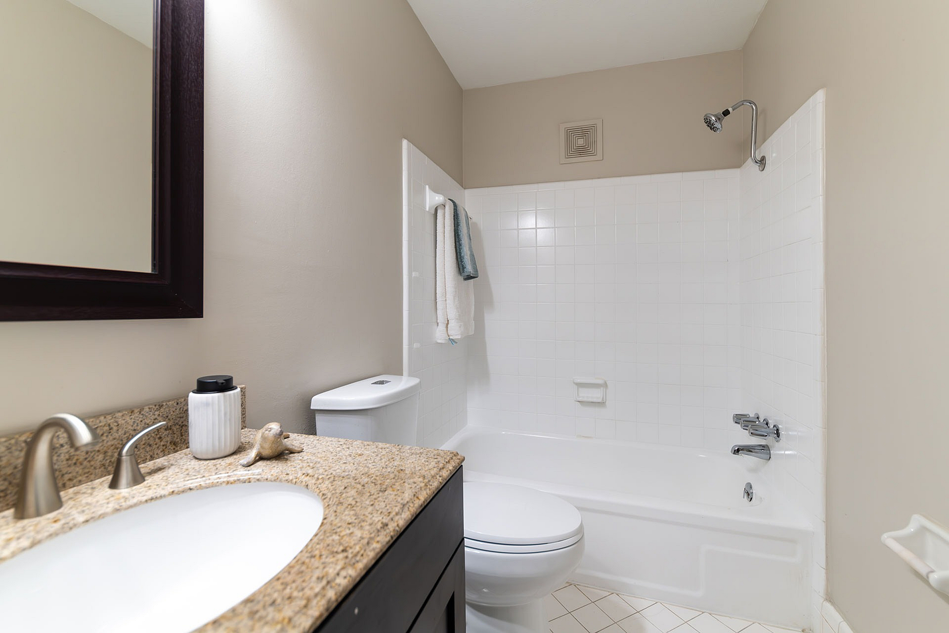 Modern bathroom featuring a sleek granite countertop, mirror, and a pristine bathtub with towels.