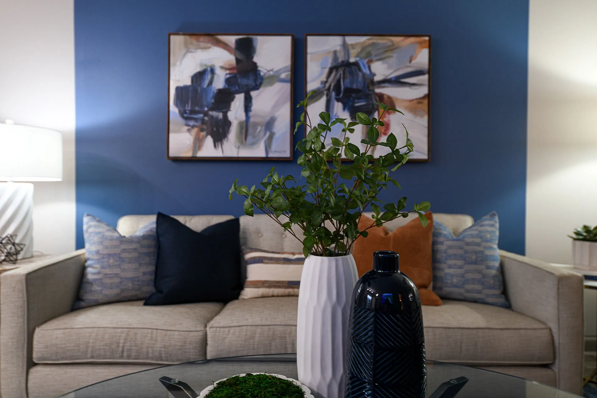 Elegant living room with a stylish beige sofa, two abstract paintings, and vibrant decor pieces.