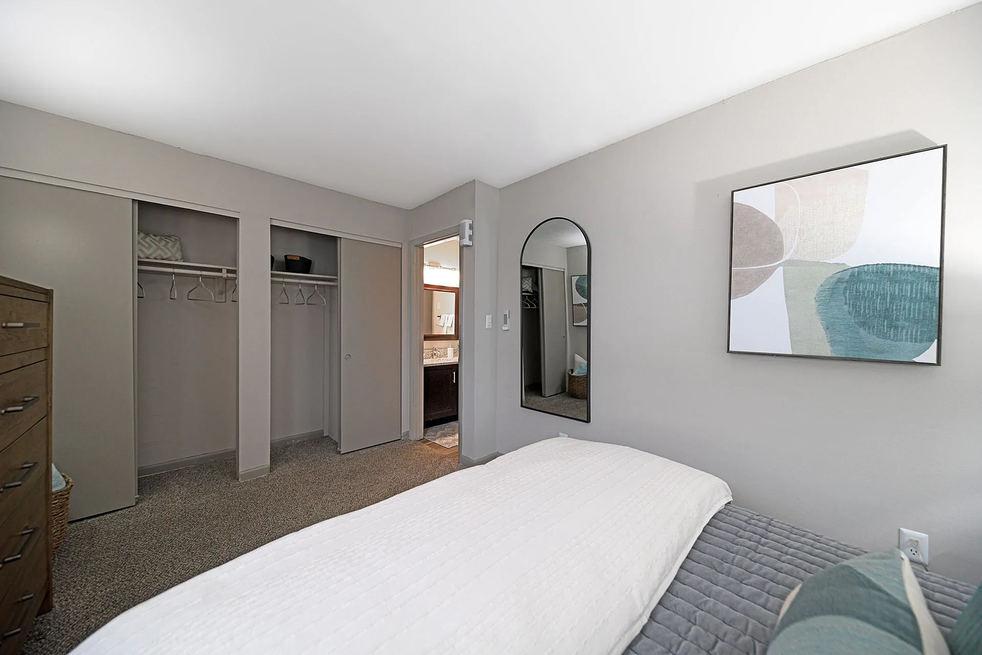 Elegant bedroom with modern decor, featuring a large closet, wall mirror, and abstract art piece.