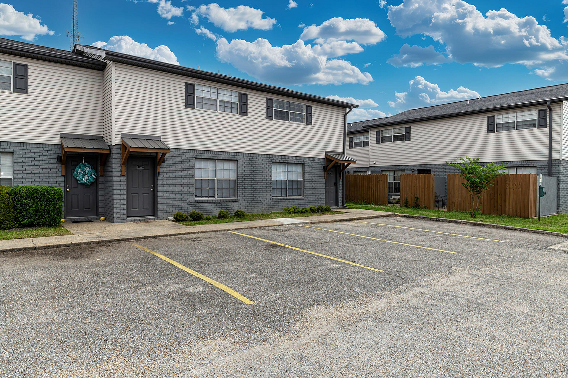 Charming two-story townhome with modern design, featuring gray and white exterior, ample parking space, and inviting curb appeal under a bright blue sky.