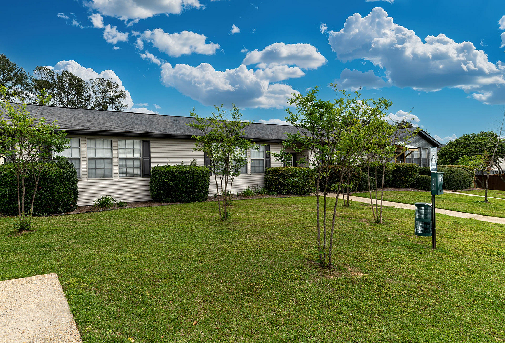Charming single-story apartment with manicured lawns, surrounded by lush greenery under a clear blue sky.