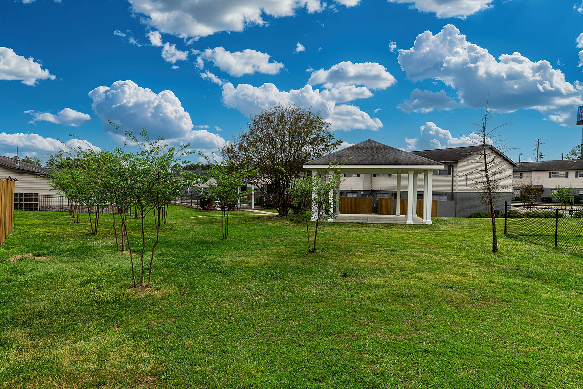 Charming backyard with lush green grass, a cozy white gazebo, and clear blue skies, perfect for relaxation and outdoor gatherings.