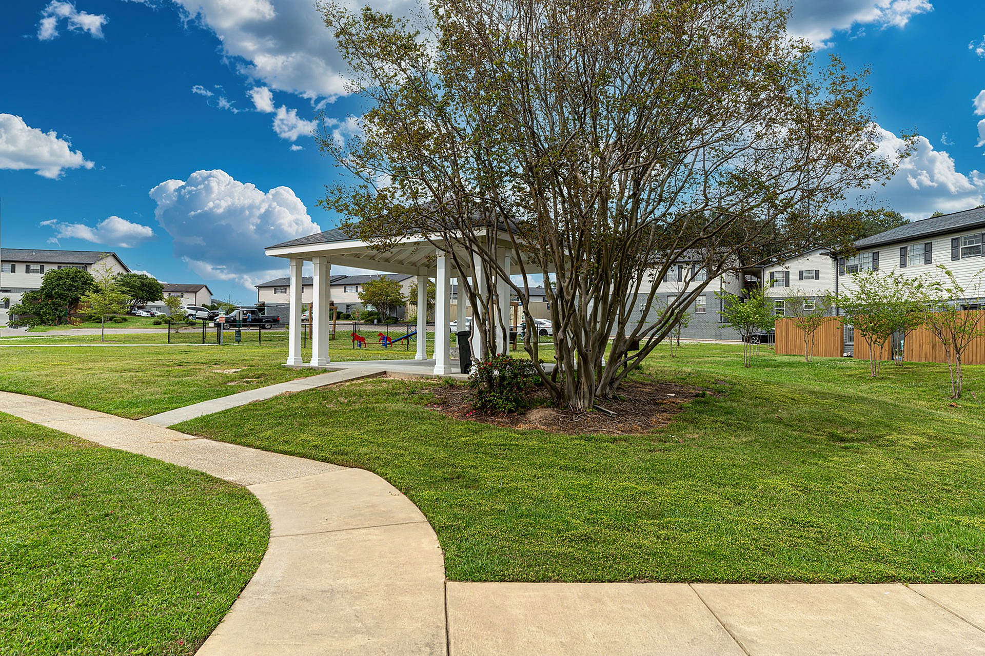 Charming residential area with lush greenery, a welcoming pavilion, and playground set against a bright blue sky.