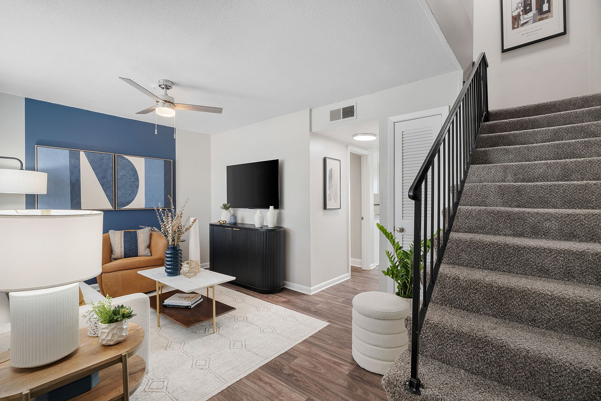 Modern living room with stylish decor, featuring a cozy seating area, sleek TV setup, and elegant staircase in a bright, open space.