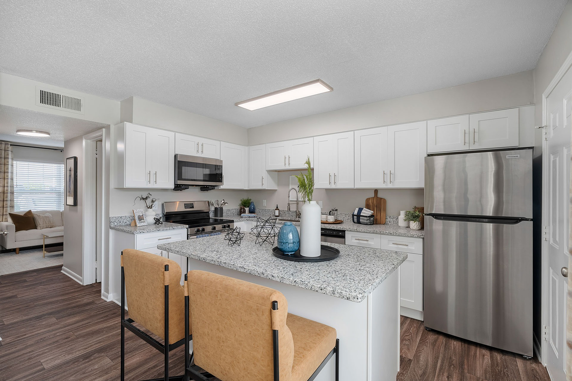 Elegant modern kitchen with sleek stainless steel appliances, granite countertops, and stylish seating, opening to a cozy and bright living area.