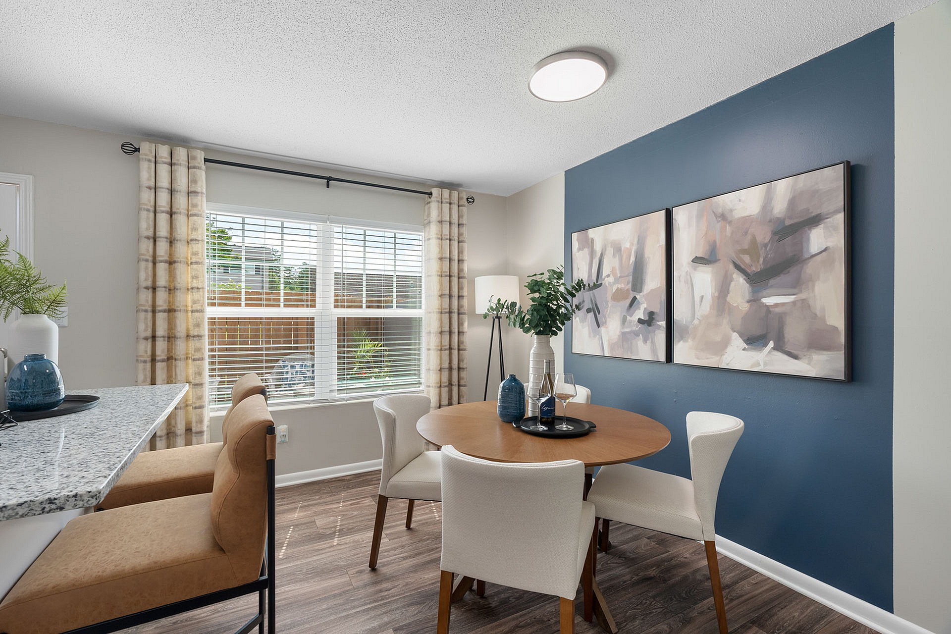 Bright dining area with modern decor, featuring a round wooden table, stylish white chairs, and a large window letting in natural light.