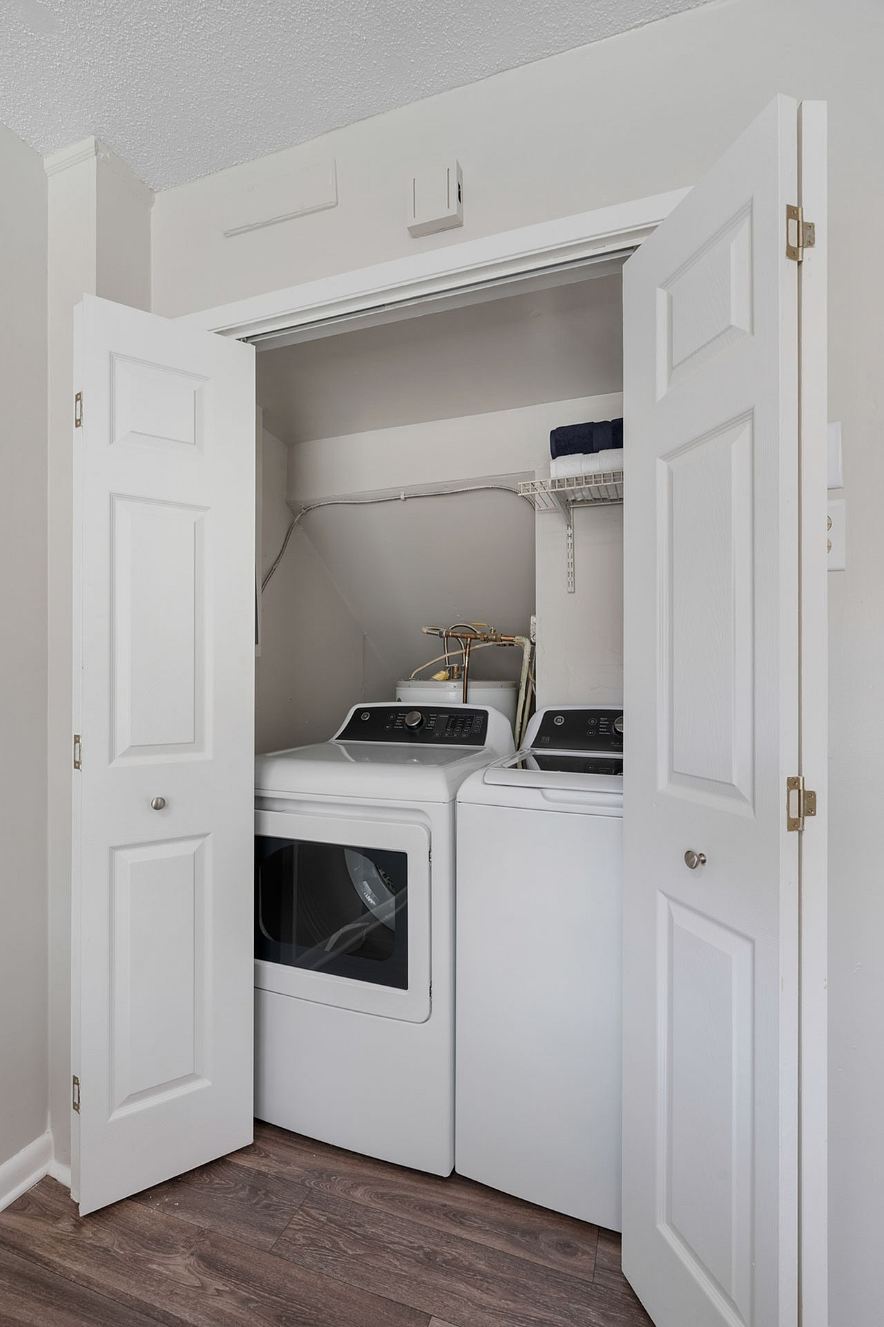 Compact laundry area with sleek washer and dryer neatly tucked behind white folding doors on elegant wood flooring.