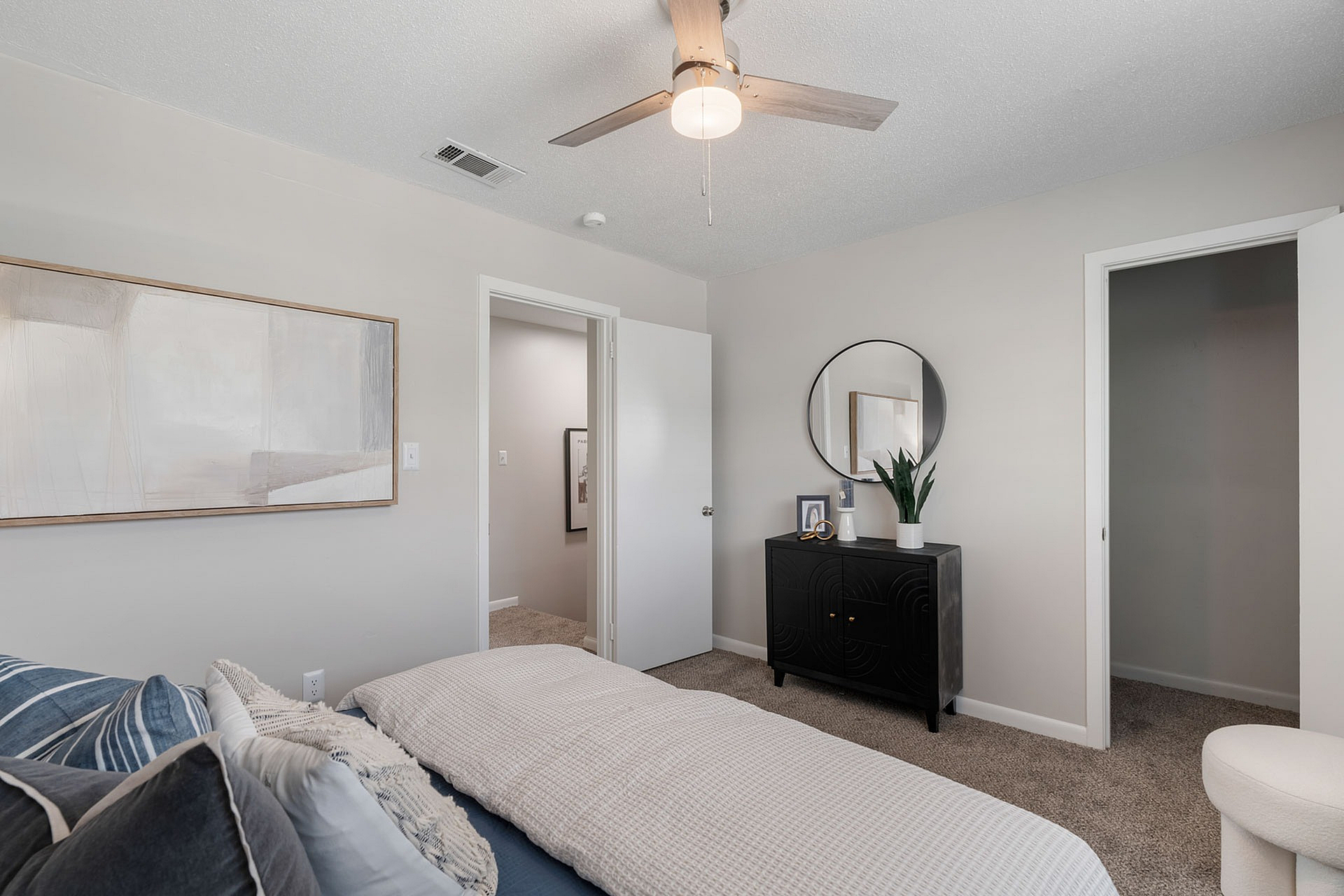 Chic bedroom with elegant decor, featuring a cozy bed, woven throw blanket, stylish dresser with a round mirror, and modern ceiling fan.