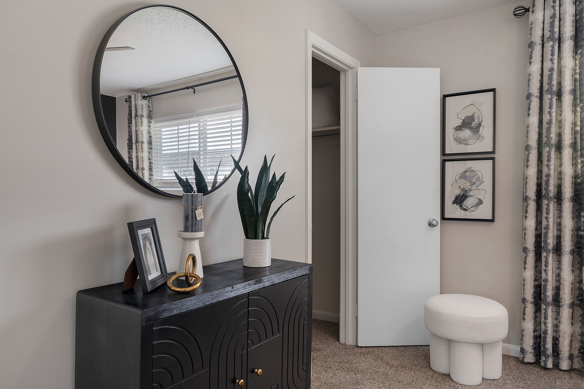 Elegant interior featuring a chic black cabinet with decorative items, a modern round mirror, and artistic wall decor in a serene bedroom setting.