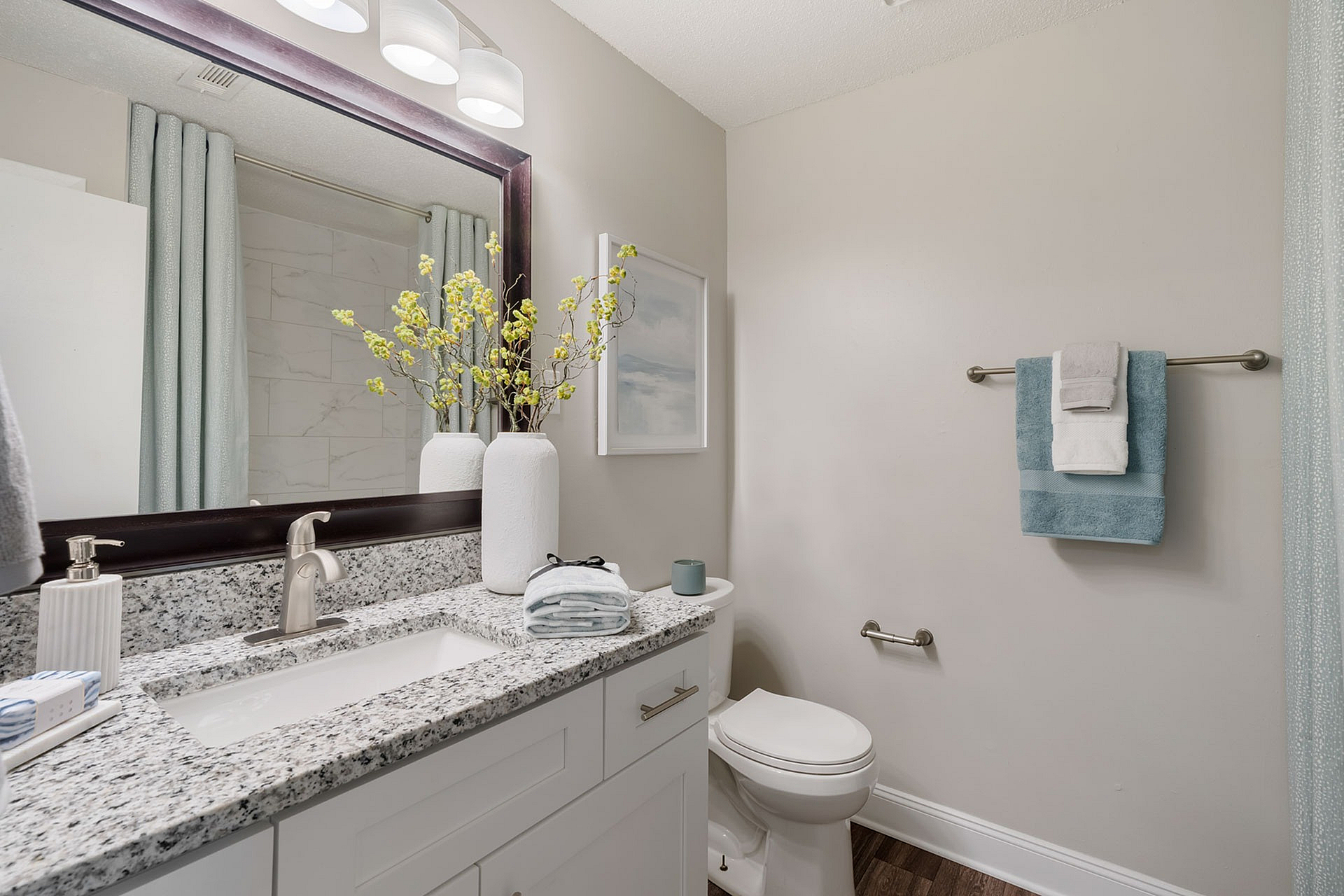 Elegant bathroom featuring granite countertop, large mirror, stylish lighting, and tasteful decor with fresh towels.