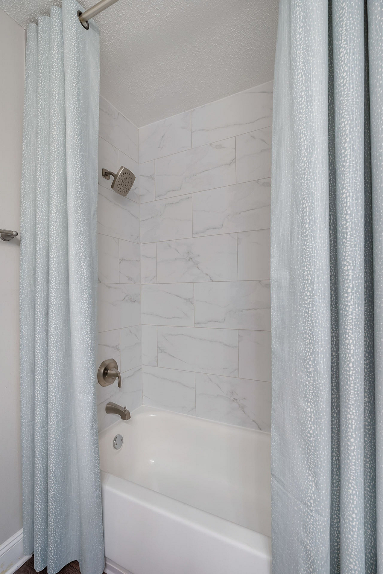 Elegant bathroom with sleek marble-tiled walls and a modern showerhead, featuring a soothing light blue shower curtain.