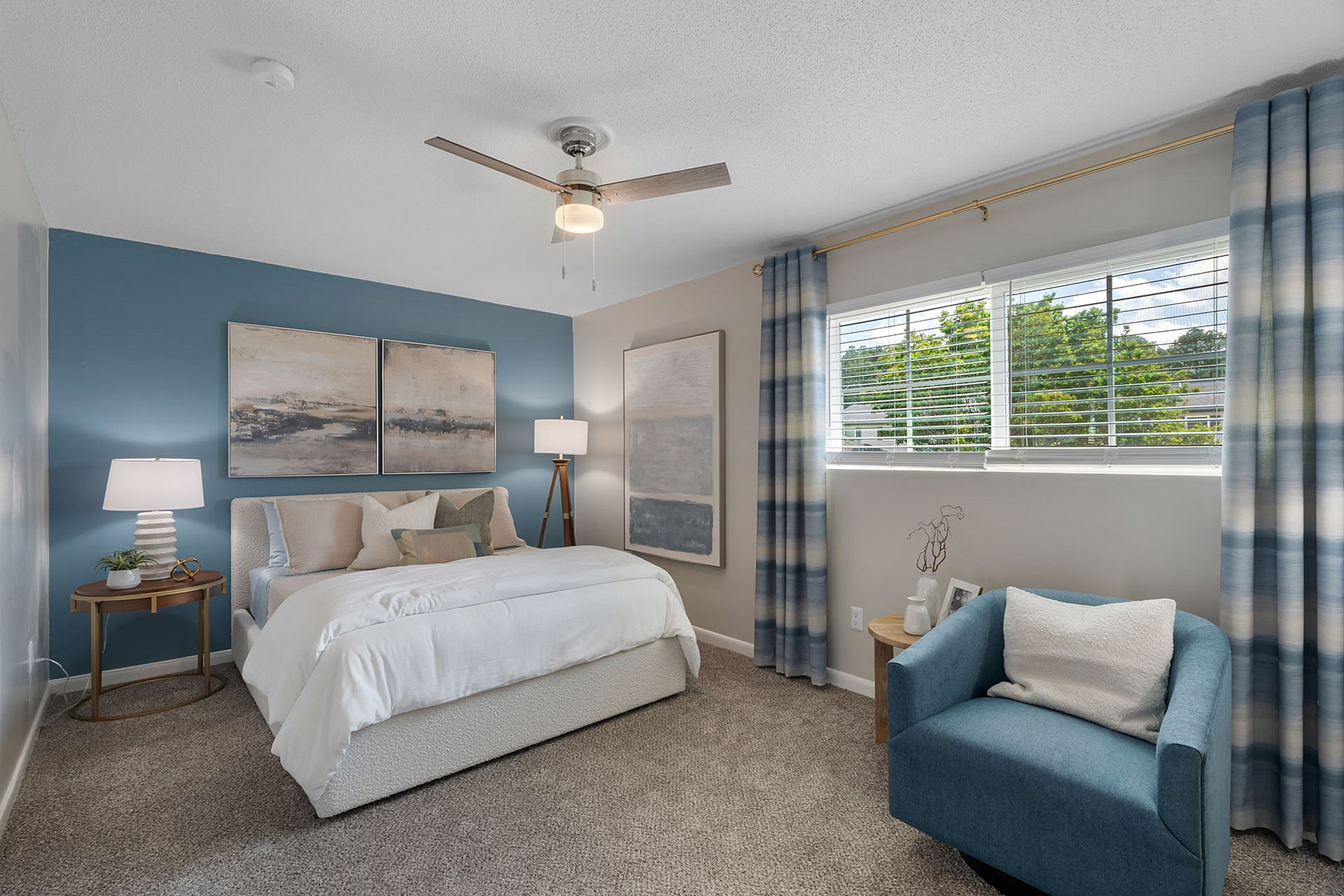 Inviting bedroom with a cozy bed, modern decor, and a serene blue accent wall. Sunlit room featuring stylish curtains and a comfortable armchair.