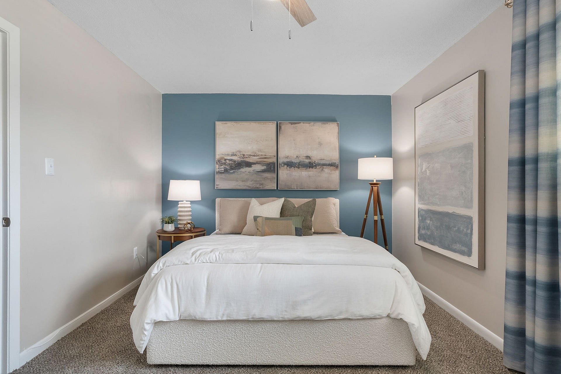 Inviting bedroom with a cozy white bed, artistic decor, and soothing blue accent wall, perfect for relaxation.