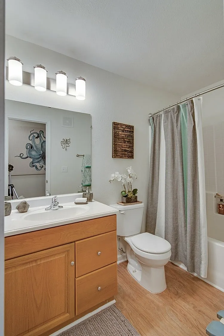 Inviting bathroom with elegant wooden cabinetry, modern light fixtures, and a stylish shower curtain. Features decorative artwork and a fresh orchid for a serene ambiance.