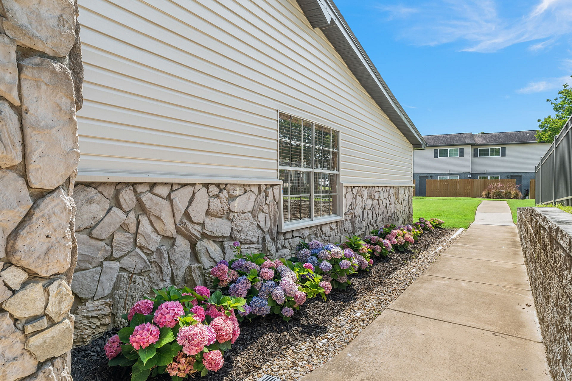 Charming exterior view of a modern house with stone and siding facade, featuring a vibrant garden of colorful hydrangeas lining a tidy walkway.