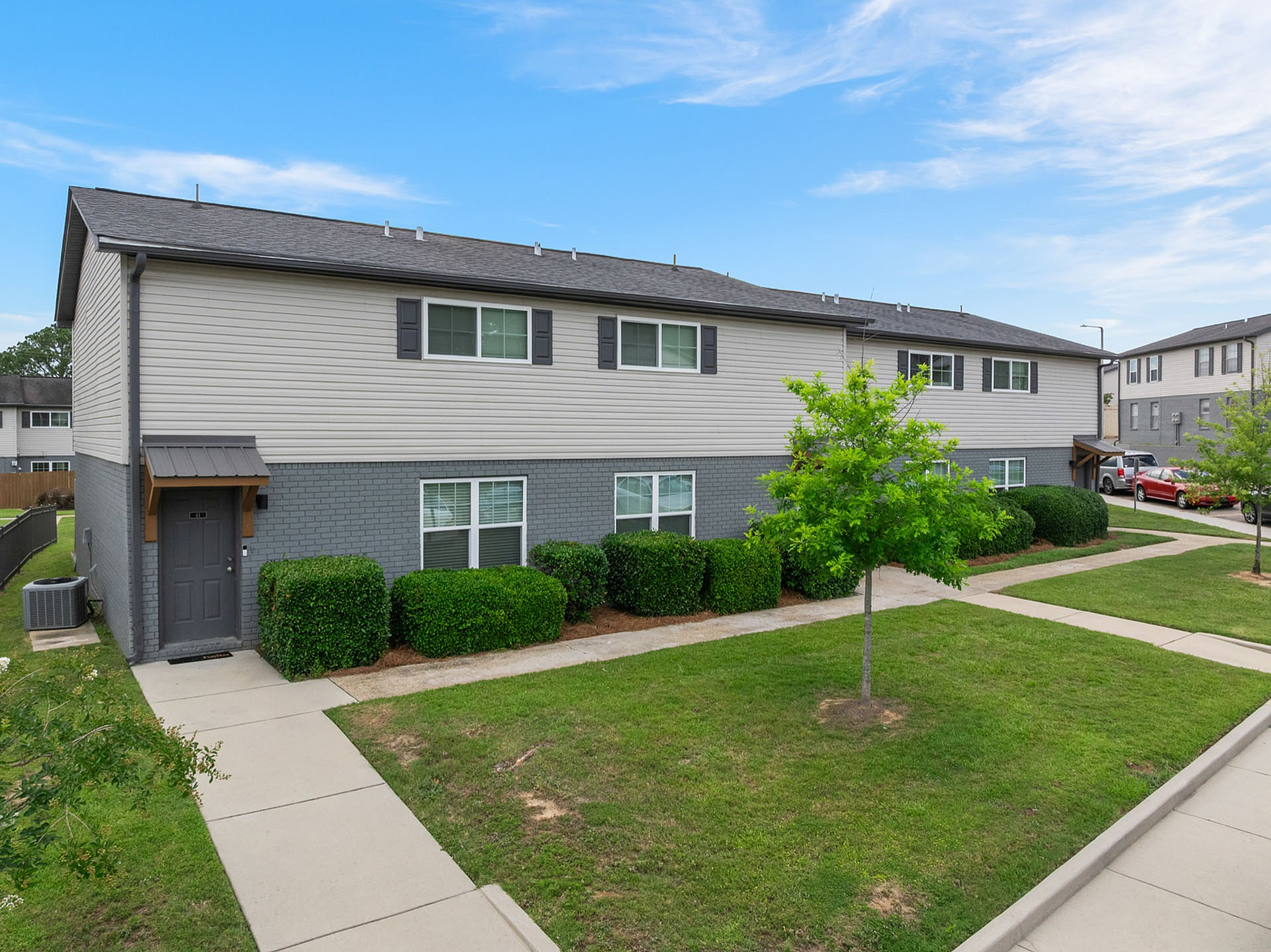 Modern two-story apartment building with a well-maintained lawn and vibrant greenery, showcasing a serene residential environment under a clear blue sky.