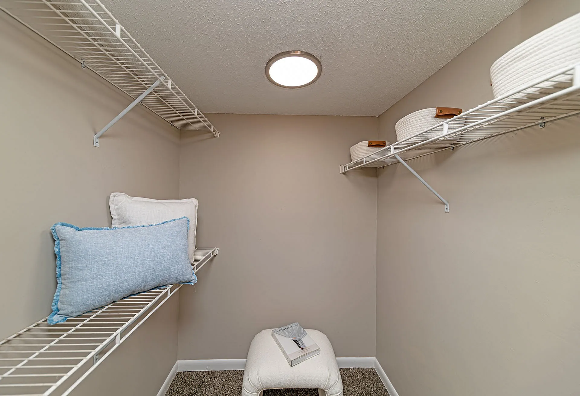 Spacious walk-in closet with modern shelving, plush seating, and elegant lighting, perfect for organized living.