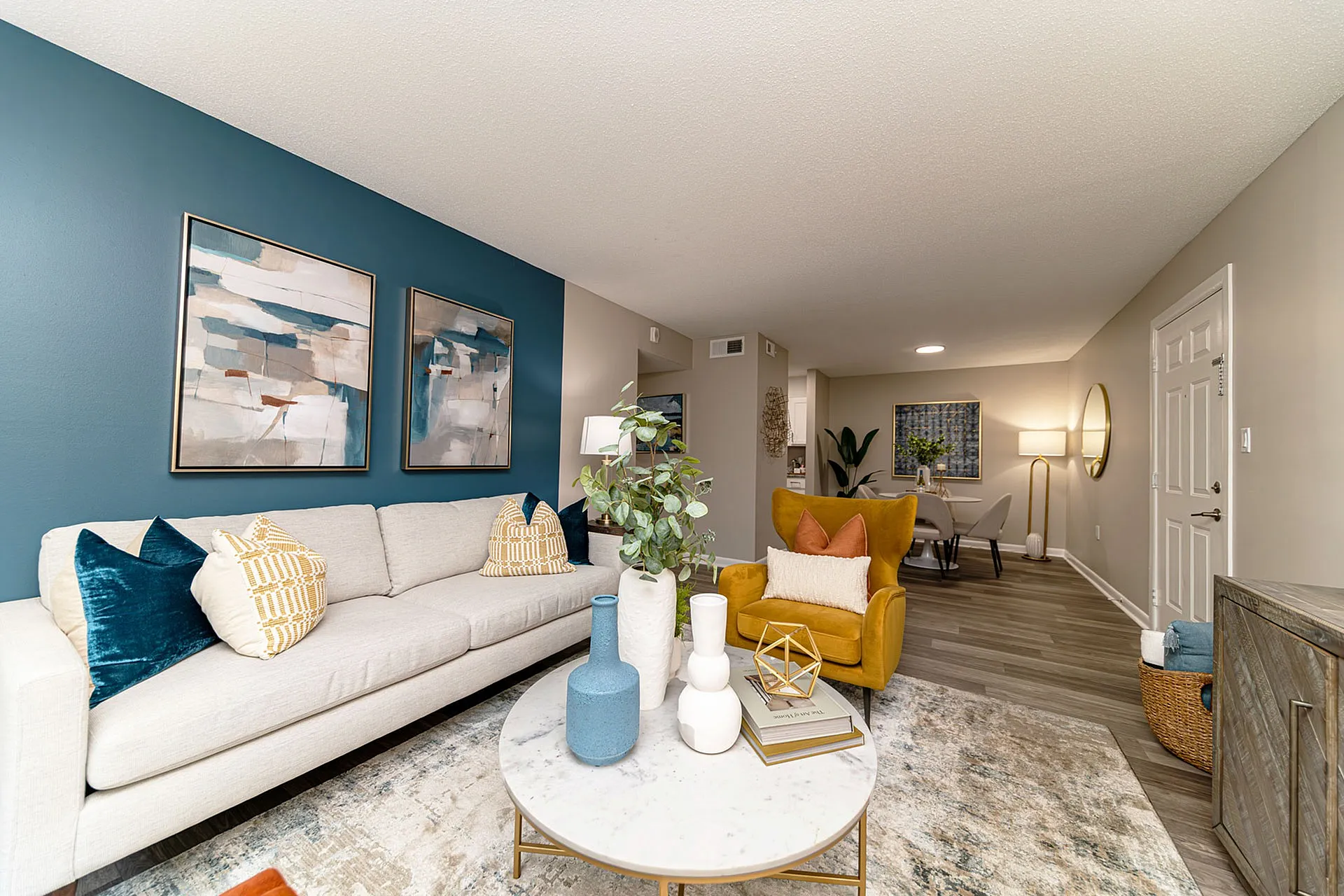 Contemporary living room with vibrant mustard armchair, modern decor, and stylish artwork, leading into a chic dining area.