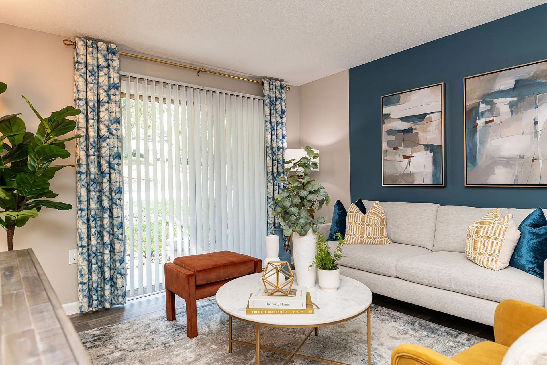 Bright, modern living room with elegant blue accent wall, cozy grey sofa, vibrant cushions, and stylish curtains framing a garden view.