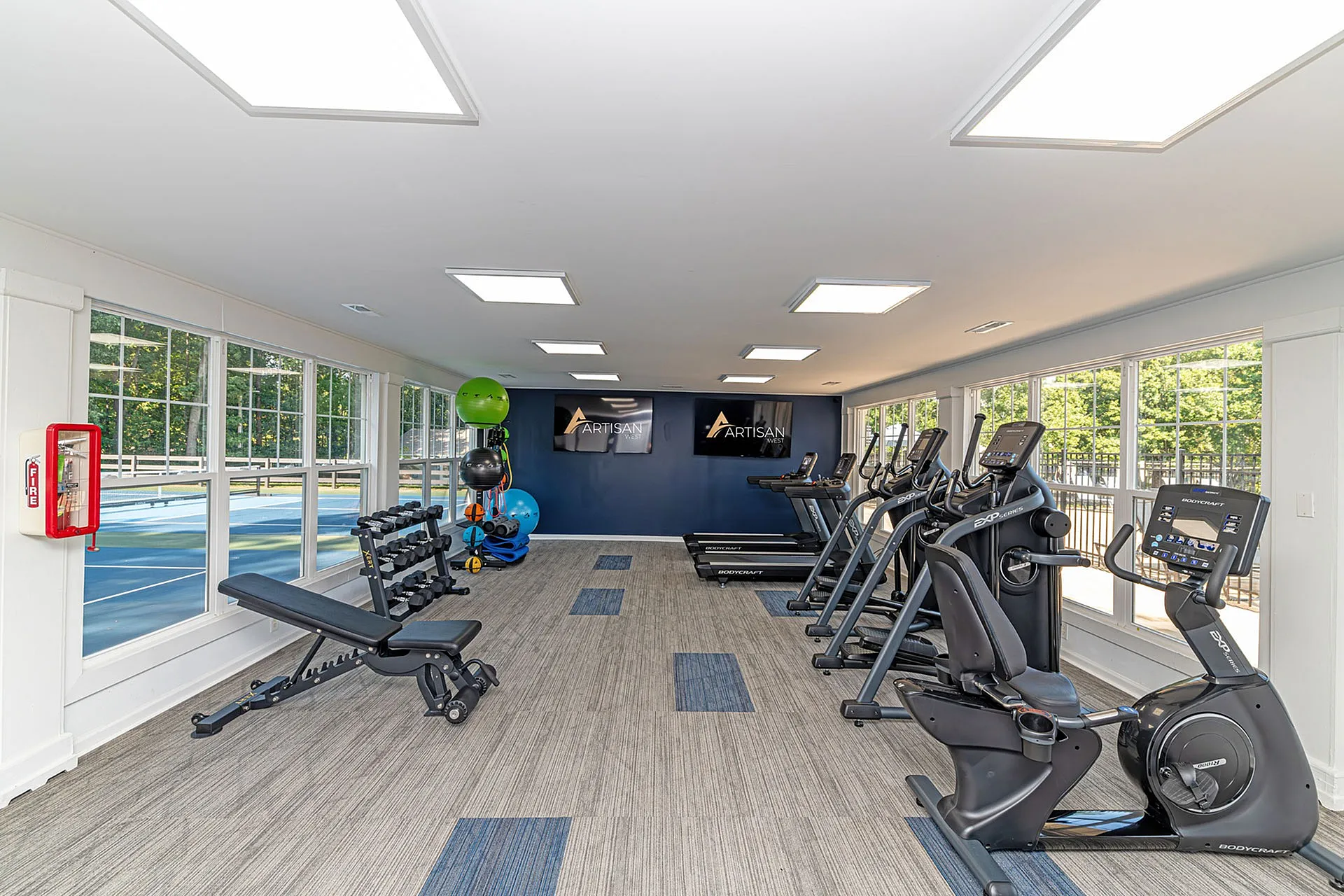 Modern fitness center with large windows, featuring treadmills, ellipticals, weight benches, and vibrant exercise balls.